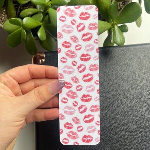 May include: White bookmark with a repeating pattern of pink and red lips.