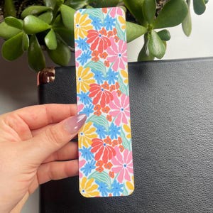 May include: A colorful bookmark with a floral pattern featuring pink, blue, yellow, and orange flowers on a white background.