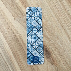 May include: Blue and white patterned bookmark with a white background and a blue floral design. The bookmark has the text "Mad Poppy" at the bottom.