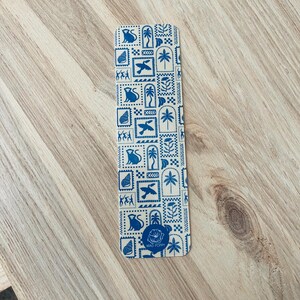 May include: A blue and white bookmark with a repeating pattern of monkeys, birds, palm trees, and geometric shapes. The bookmark has the text "MAD POPPY" at the bottom.