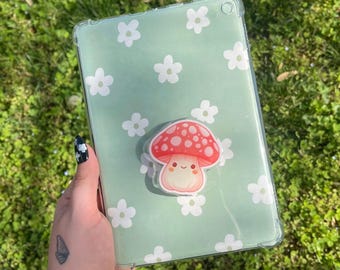 May include: A clear green phone case with a white daisy pattern. A red and white mushroom with a smiling face is on the case.