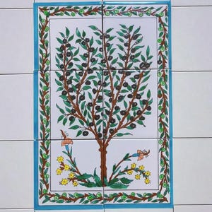 May include: A decorative tile mural featuring a stylized olive tree design. The tree has a brown trunk, green leaves, and black olives. The mural is framed with a blue border and floral accents. The tiles are mounted on a white tiled wall.