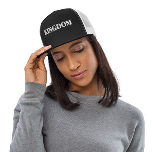 May include: Black and white trucker hat with the word "KINGDOM" in white block letters. The hat has a black front panel and brim, with a white mesh back. The brim is slightly curved.