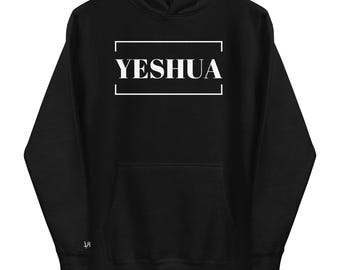 May include: Black hoodie with a front pocket and a hood. The word "YESHUA" is printed in white inside a white rectangular frame. The hoodie has a drawstring and a small logo on the left sleeve.