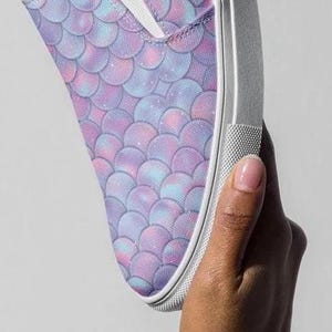 Puede incluir: Un par de zapatos de lona blancos de deslizamiento con un patr&oacute;n de escamas de sirena p&uacute;rpura y azul.