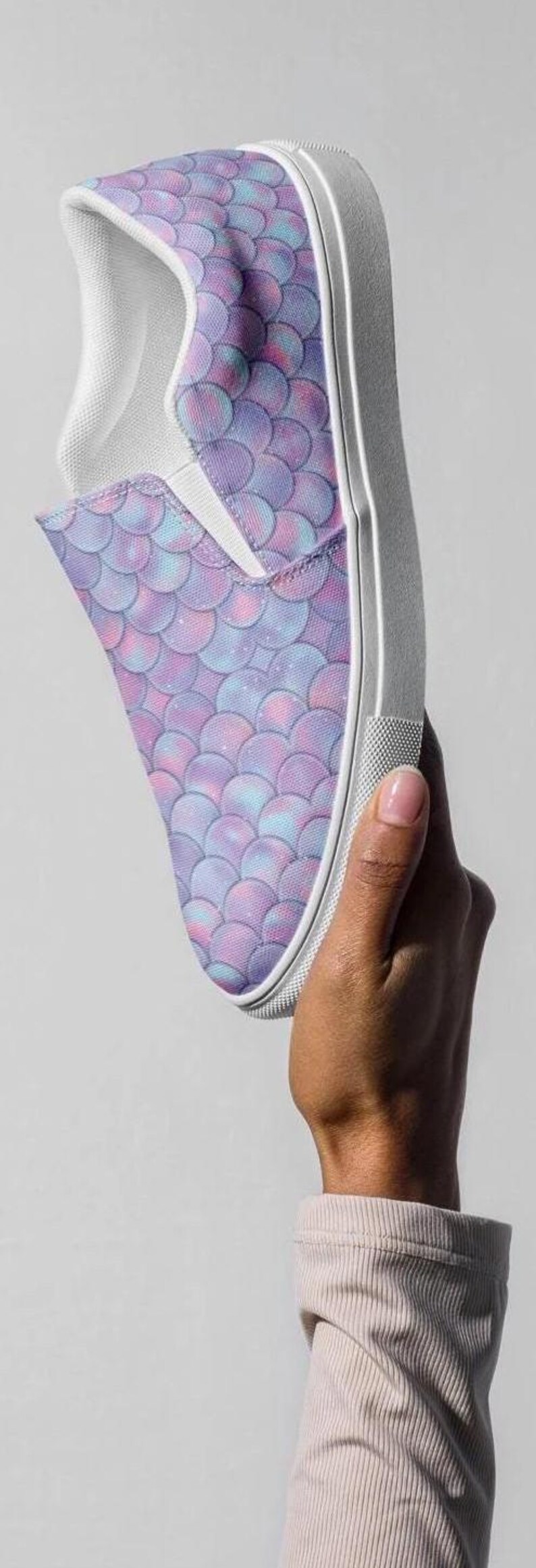 Puede incluir: Un par de zapatos de lona blancos de deslizamiento con un patr&oacute;n de escamas de sirena p&uacute;rpura y azul.