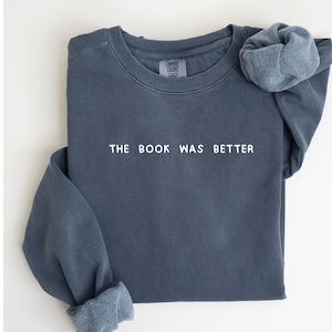 May include: A dark blue sweatshirt with the text "THE BOOK WAS BETTER" printed in white on the front.