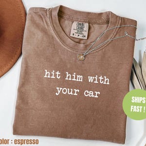 以下が含まれることがあります： エスプレッソブラウンのTシャツに、白い文字で「hit him with your car」とプリントされています。