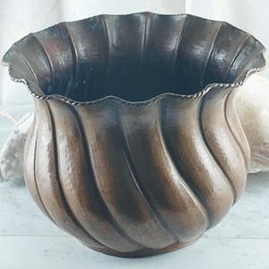 May include: A large, antique copper bowl with a wavy, textured exterior. The rim has a decorative, scalloped edge. The bowl's interior is dark, and the exterior has a rich, brown patina. A decorative piece for the home.