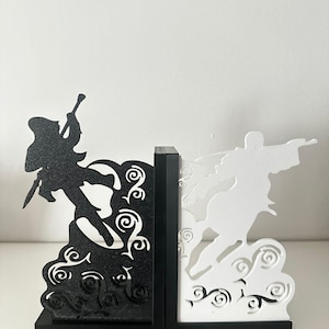 May include: Black and white decorative bookends featuring stylized figures in action poses. The bookends have a black and white color scheme, with intricate cloud and swirl designs at the base. The figures appear to be engaged in a dynamic, action-oriented scene.