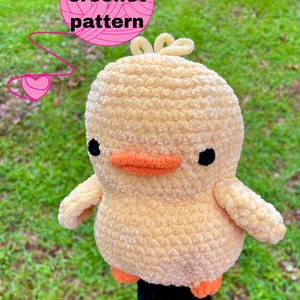 以下が含まれることがあります： 黒い目、オレンジ色のくちばし、オレンジ色の足を持つ、黄色いアヒルのゴルフクラブヘッドカバーを編んでいます。カバーはゴルフクラブのシャフトに取り付けられています。テキスト「PDF crochet pattern」は、ピンクの糸玉にピンクの文字で書かれています。