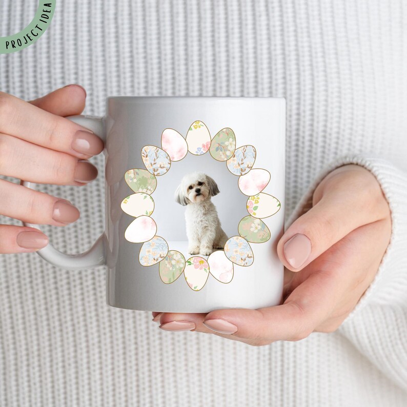 Pu&ograve; includere: Tazza in ceramica bianca con un piccolo cane bianco e soffice al centro, circondato da una ghirlanda di uova di Pasqua dai colori pastello. La tazza ha un manico curvo e le parole "PROJECT IDEA" in verde. Il design &egrave; centrato, creando un tema festivo e stagionale.