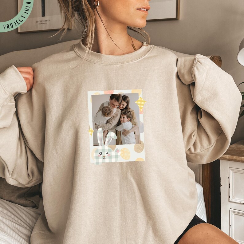 Pu&ograve; includere: Felpa beige con una foto di famiglia in una cornice in stile polaroid. La cornice &egrave; decorata con elementi a tema pasquale, tra cui un coniglietto e uova dai colori pastello. La felpa &egrave; di colore neutro, adatta per un abbigliamento casual.