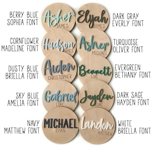 K&ouml;nnte beinhalten: Eine Sammlung personalisierter Namensschilder aus Holz. Jedes runde Schild zeigt einen Namen in verschiedenen Farben und Schriftarten, mit einem kleineren Namen darunter. Der Text enth&auml;lt Namen wie Asher, Elyah, Hudson und Bennett. Die Schilder sind in verschiedenen Farben.