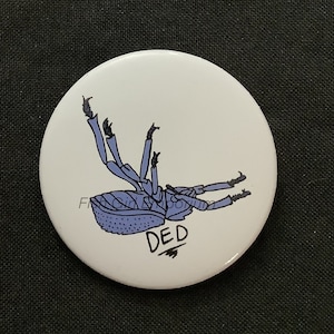 Könnte beinhalten: Ein weißer Knopf mit einer blauen und schwarzen Illustration eines Käfers mit dem Wort "DED" darunter.