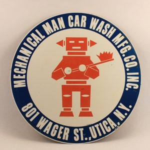 May include: A blue and white circular sign with the text "Mechanical Man Car Wash Mfg. Co. Inc. 801 Wager St. Utica, N.Y."  The sign features a red robot holding a brush.