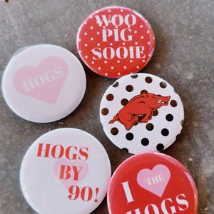 May include: A collection of five round buttons with various designs. One button is red with white polka dots and the text "WOO PIG SOOIE." Other buttons feature hearts and the word "HOGS" in pink and white.