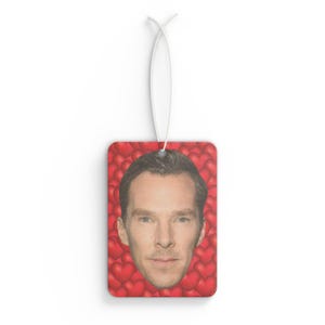 May include: A red car air freshener with a man's face surrounded by red hearts.