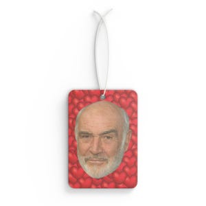 May include: A red car air freshener featuring a man's face surrounded by red hearts.