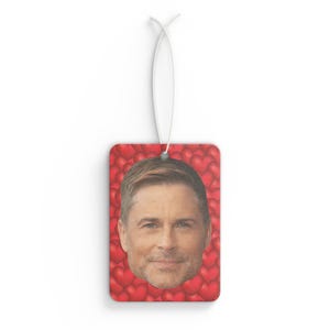 May include: A red car air freshener featuring a man's face surrounded by red hearts.