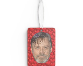 May include: A car air freshener with a red heart pattern and a photo of a man's face in the center.