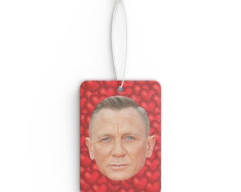May include: A red car air freshener with a man's face on it. The face is surrounded by red hearts.
