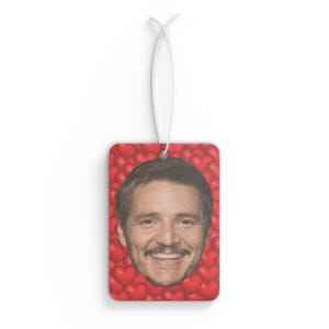 May include: A red car air freshener with a man's face surrounded by red hearts.