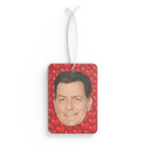 May include: A red car air freshener with a photo of a man's face surrounded by red hearts.