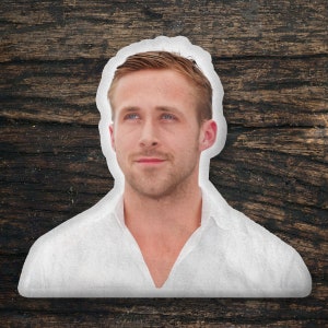 May include: A cutout image of a man with fair skin, blue eyes, and light brown hair, wearing a white collared shirt. The image is set against a dark brown, textured wooden background.