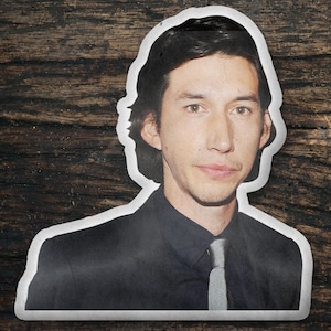 May include: A man with dark hair and a dark suit jacket, wearing a light gray tie. He has a serious expression on his face.