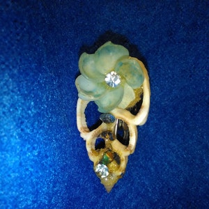 May include: A white seashell brooch with a blue flower and rhinestones. The flower has a light blue center with a clear rhinestone in the middle.