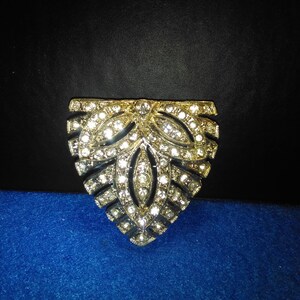 May include: A gold-toned brooch with a triangular shape and a design of stylized leaves set with clear rhinestones.