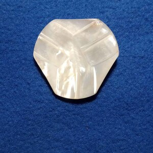 May include: A white iridescent shell with a carved design. The shell is shaped like a leaf and has a smooth, polished surface.