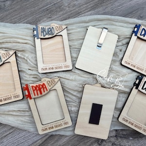 May include: Set of six wooden photo frames with a pennant design. Each frame features a different title, including "Best Grandpa Ever", "Best Abuelo Ever", "Best Papa Ever", and "Best Dad Ever". The frames are made of natural wood and have a rustic look. Each frame includes the text "Happy Father's Day from your biggest fans!"