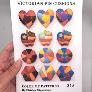 Peut inclure: Un livre intitulé "Victorian Pin Cushions" présentant des modèles de coussins à épingles en patchwork en forme de cœur, de pomme, de cercle et d'hexagone. Les motifs sont multicolores et comprennent des étoiles et des rayures. Le livre est de Shirley Stevenson et porte le numéro 345.