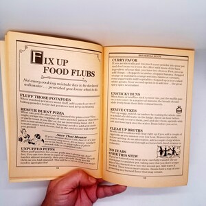 May include: Open cookbook page with the title "Fix Up Food Flubs" and household hints. The page features text with cooking tips and advice, with illustrations of food and cooking utensils. The book is open on a wooden table.