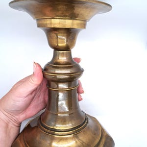 May include: A vintage brass candlestick with a wide, flared top and a detailed, ornate base. The candlestick has a warm, golden hue and a classic design. The overall height is approximately 10 inches.