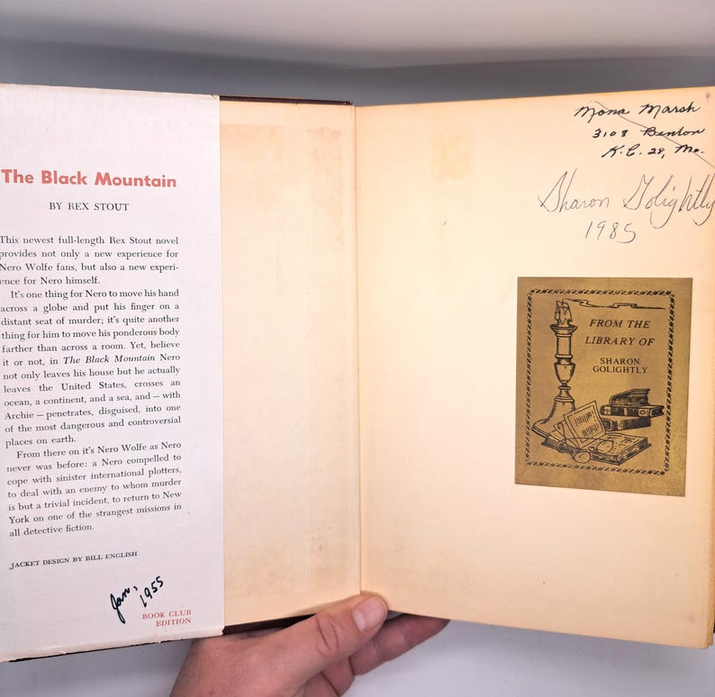 Puede incluir: Un libro abierto titulado "The Black Mountain" de Rex Stout, con texto y un sello de edici&oacute;n del club de lectura. La contraportada interior presenta una inscripci&oacute;n manuscrita y una etiqueta de biblioteca de Sharon Golightly.