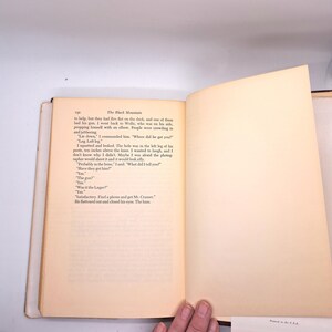 Puede incluir: Un libro abierto con texto en la p&aacute;gina izquierda y una p&aacute;gina derecha en blanco. El texto se titula "The Black Mountain" e incluye di&aacute;logos. Las p&aacute;ginas son de color blanquecino con un lomo marr&oacute;n. Una mano es visible en la parte inferior.