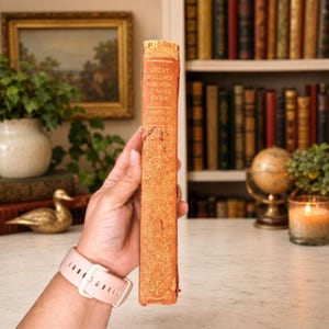 May include: A vintage orange hardcover book titled Great Speeches and How to Make Them by Grenville Kleiser. The spine features intricate gold-colored embossed floral patterns and lettering, showing signs of wear along the edges and corners.
