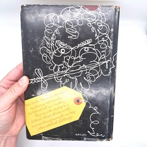 Puede incluir: Una portada de libro vintage con un fondo negro y arte lineal abstracto blanco. Una etiqueta amarilla con texto est&aacute; adjunta a la portada. El texto de la etiqueta dice "Nero Wolfe breaks all precedent..." y contin&uacute;a con una descripci&oacute;n de la trama del libro.