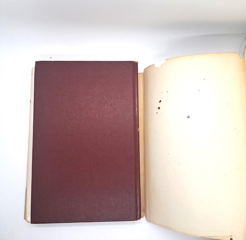 Puede incluir: Un libro abierto con una cubierta burdeos y p&aacute;ginas envejecidas de color blanquecino. La cubierta es s&oacute;lida y lisa, mientras que las p&aacute;ginas muestran signos de edad con peque&ntilde;as manchas y un borde ligeramente rasgado. El libro est&aacute; sobre un fondo blanco.