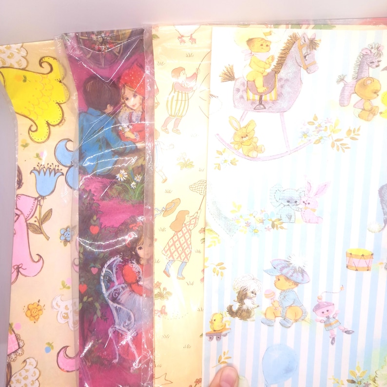 May include: Three sheets of decorative wrapping paper featuring vintage-style illustrations. One sheet displays children and flowers on a yellow background, another shows a dark pink scene with figures, and the third features blue stripes with toys.