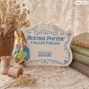 May include: A white ceramic plaque with a scalloped edge featuring a raised, painted figure of Peter Rabbit holding carrots. The text reads Beatrix Potter Collectibles and Schmid in blue, surrounded by a delicate blue vine and floral border design.
