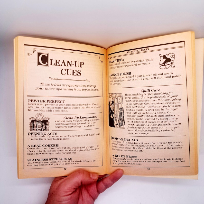 May include: Open book with household hints and cleaning tips. The pages are yellowed, and the text is in black. The book is open to pages 52 and 53, with headings like "Clean-Up Cues" and "Quilt Care."
