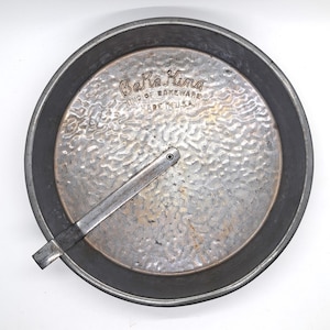 May include: A round, silver-toned Bake King cake pan with a textured interior and a handle. The pan has the words "Bake King" and "King of Bakeware Made in U.S.A." embossed on the surface.
