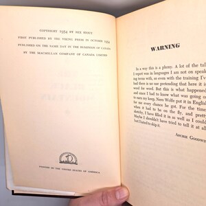 Puede incluir: Libro abierto con texto, incluyendo "COPYRIGHT 1954 BY REX STOUT" y "WARNING". Las p&aacute;ginas son de color blanquecino con texto negro. El libro est&aacute; abierto en una p&aacute;gina con texto y un peque&ntilde;o emblema en la parte inferior. Una mano sostiene el libro.