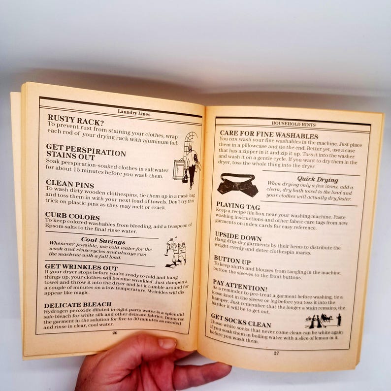 May include: Open book with laundry tips, including stain removal, washing instructions, and fabric care. The pages are yellowed, with text and illustrations. The book is held open by a hand.