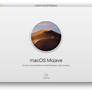 May include: A computer screen displays the macOS Mojave installation setup. The screen features a circular image of desert dunes under a blue sky. The text "macOS Mojave" is below the image, with instructions to click "Continue."