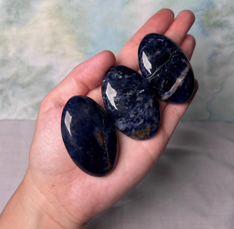 Puede incluir: Tres piedras de sodalita azul lisas de forma ovalada con vetas blancas. Las piedras est&aacute;n pulidas y tienen un acabado brillante.